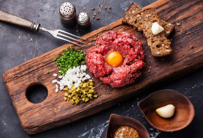 Photo d'un Tartare de Boeuf au Poivre de Kampot. Ce tartare de bœuf revisité marie la tradition française avec les saveurs puissantes du Poivre de Kampot, sublimé par une touche de Paprika Fumé.