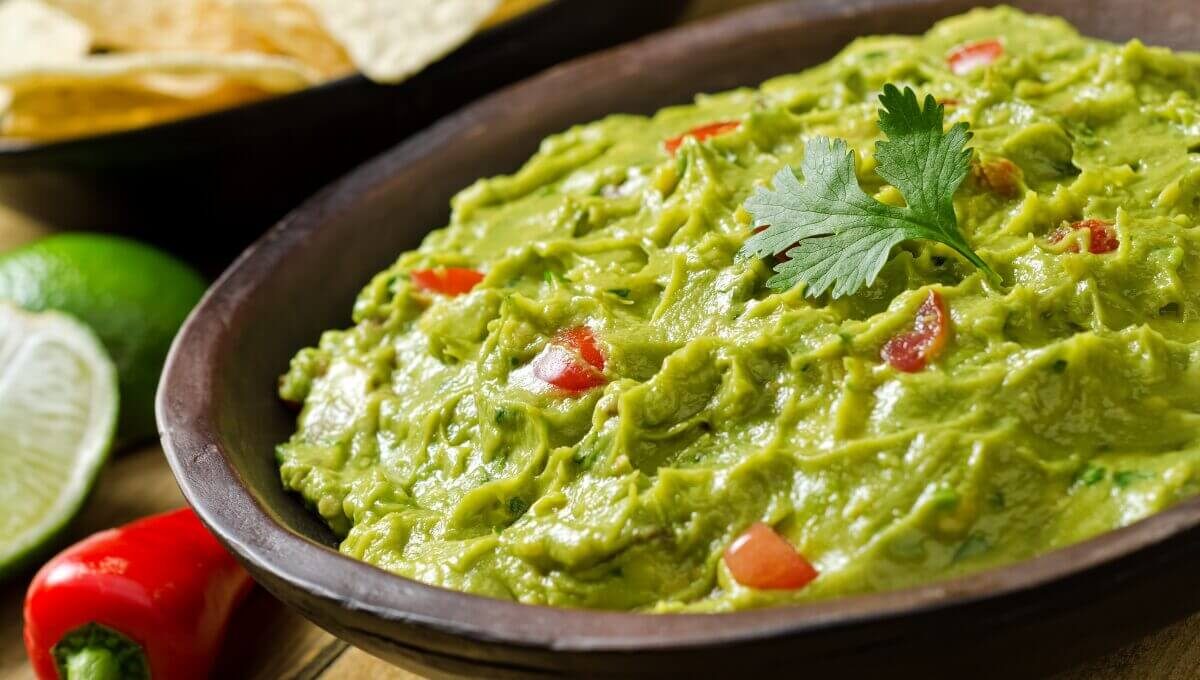 Mélange guacamole frais garni de coriandre, accompagné de piments rouges et citron vert
