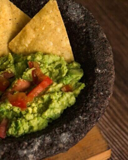 Mélange guacamole crémeux servi dans un mortier volcanique noir avec chips de maïs dorées